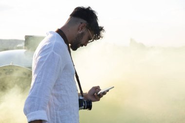 Kahverengi saçlı ve sakallı beyaz çocuk cep telefonuna bakıyor.
