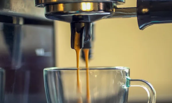 Cerrar dos corrientes de café espresso espumoso se vierten en una taza de café de cristal de la bocina de las cafeteras —  Fotos de Stock