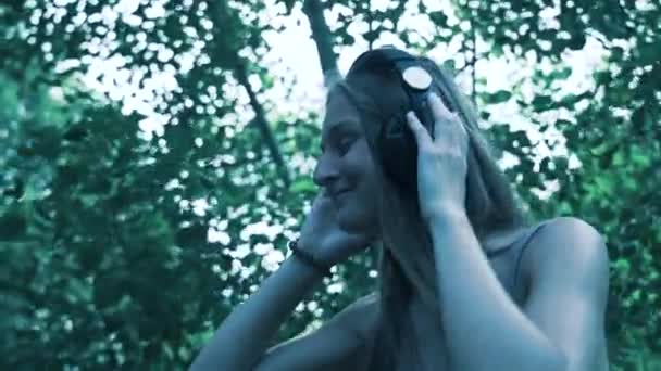 Hermosa chica joven con auriculares en la naturaleza escuchando música — Vídeos de Stock