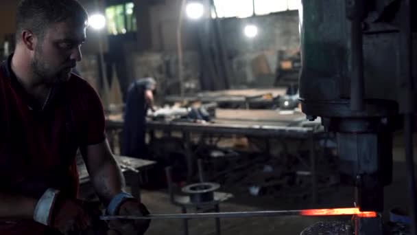 Um ferreiro forja um tarugo de metal quente vermelho com um martelo de ferreiros — Vídeo de Stock