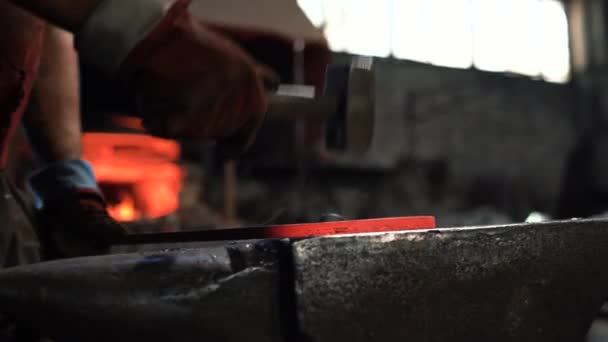 En smed använder en handhammare på ett städ för att smida en het metallprodukt — Stockvideo