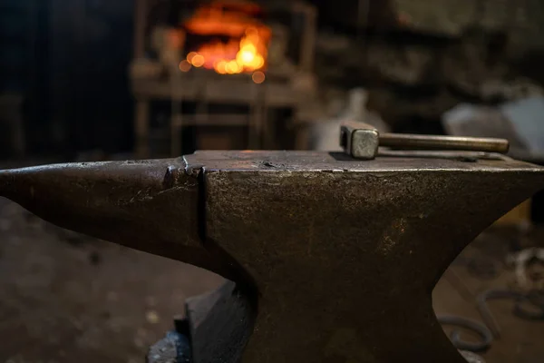 A blacksmiths hammer lies on an anvil against the background of a burning forge — Stock Photo, Image