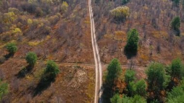 Yaprak düşüşü sırasında bir sonbahar ormanında toprak bir yol üzerinde bir uçuşun havadan videosu.