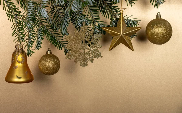 New year\'s toys of Golden color hang on a branch of a Christmas tree on a Golden background, a card for new year and Christmas