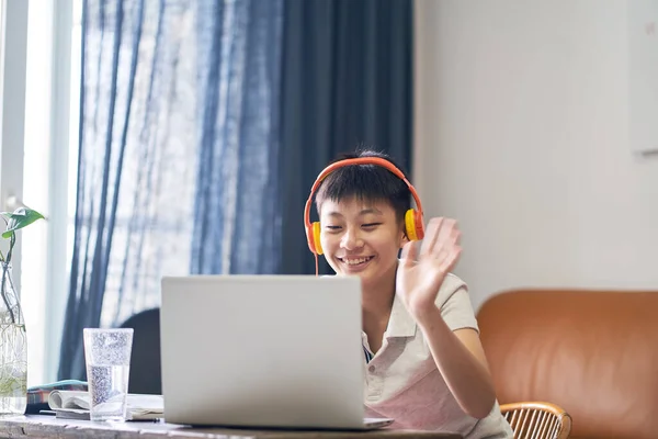 Asyalı çocuk evde online ders alıyor. Gülümsüyor ve kulaklık takıyor.
