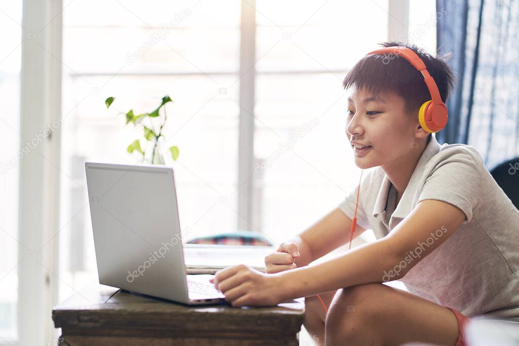 Asian kid taking online class at home smiling & wearing headset