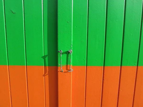 a green and orange painted wooden door with a little hook