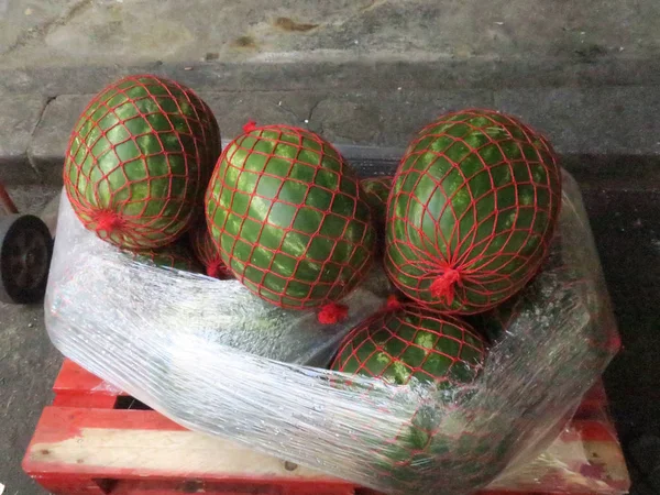Tři melouny vodní, balené v červených sítích a v plastové pokládce Stock Snímky