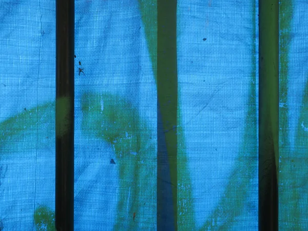 Portão de ferro coberto com um pedaço de lona de plástico azul — Fotografia de Stock