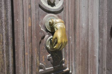 Kapı tokmağı, kahverengi ahşap kapılı süslemeleri olan bakır bir el.