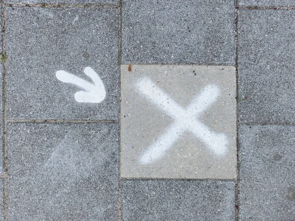 a sidewalk wit ha white painted cross and white arrow