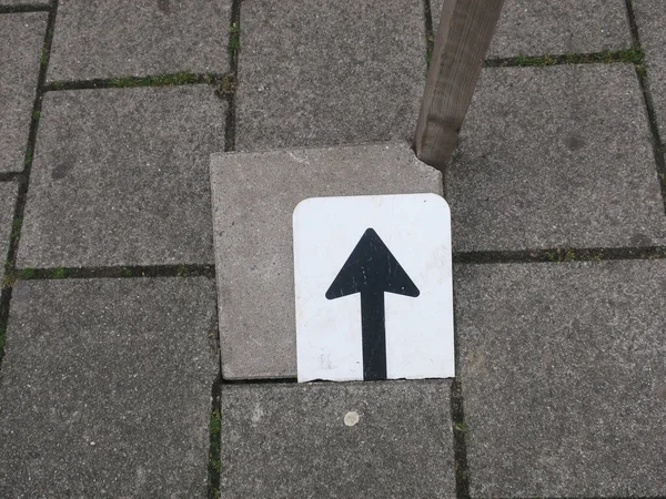 an arrow on a brokne sign on a tile on the sidewalk