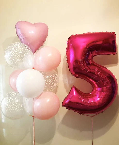 The composition of helium balloons is white, pink, transparent with confetti and a large figure of five fuchsia. Birthday present for a little princess