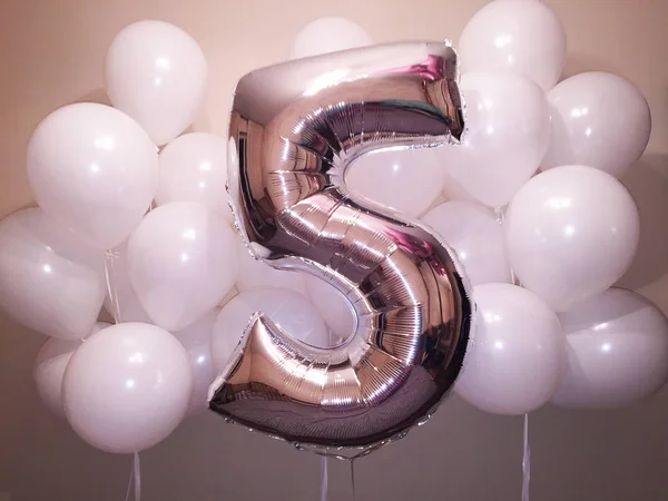 A beautiful composition of helium balloons of white color and a large figure of five silvery colors. Birthday present for a little girl