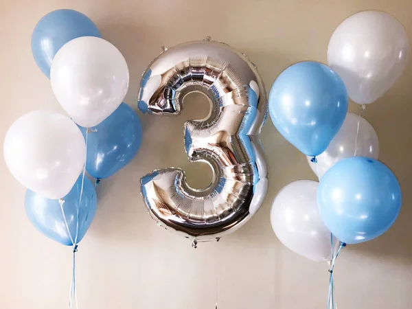 Composition of helium balloons of blue and white, as well as a silver numeral three. Gift for the birthday of his son
