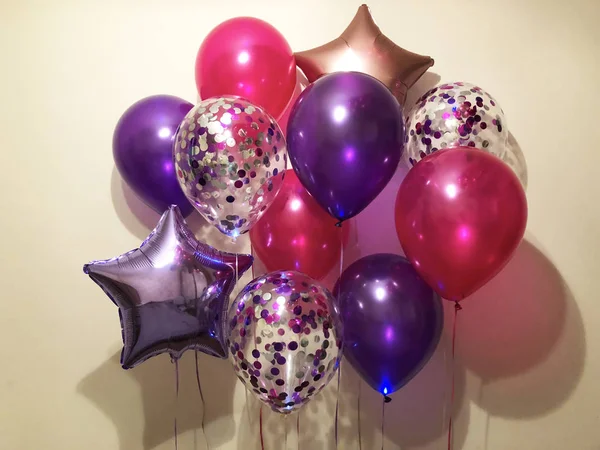 Arrangement of bright helium balloons in purple, fuchsia, transparent with confetti, as well as stars of purple metallic and rose gold