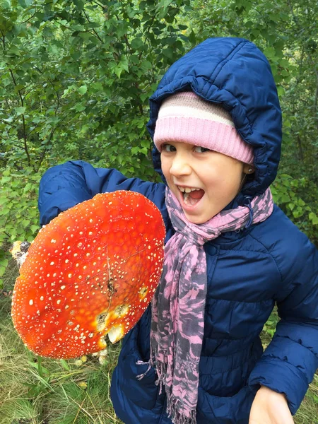 A little girl found a big red mushroom in the forest