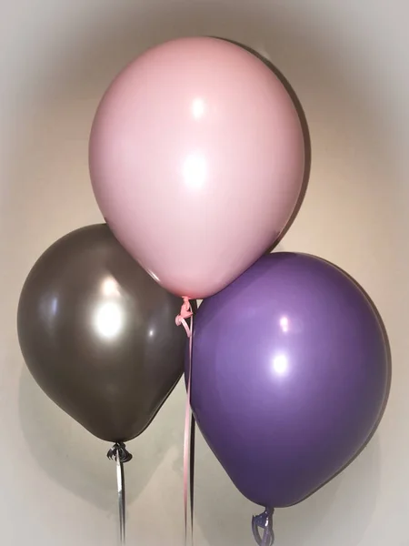 Three helium balloons in dark gray, purple and pink