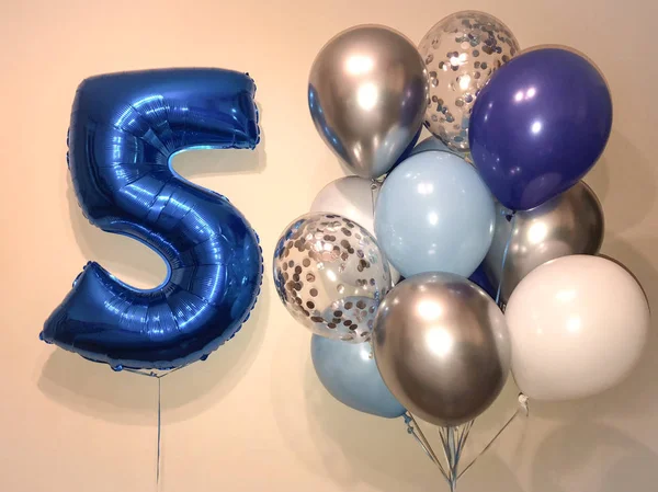 A bright composition of helium balloons of blue, silver, transparent with confetti and a large blue number five