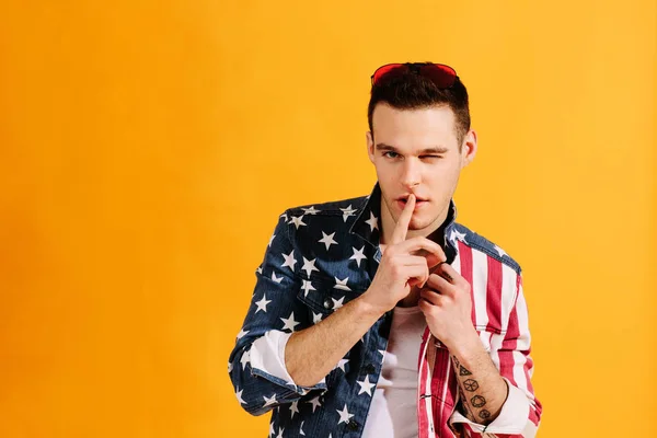 Cute guy with finger on mouth and one eye winking in american flag jacke