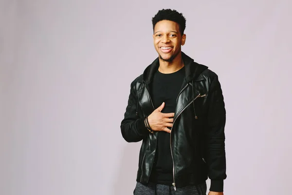 Göğsünde tek elle gülen serin genç adam siyah deri ceketli. gri arka plan üzerinde izole