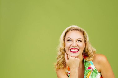 Portrait of a beautiful blonde woman with big smile and hand under chin looking up, isolated on green studio background clipart