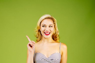 Bu, işaret ve yan, yeşil studio arka plan üzerinde izole isteyen çizgili Bikini güzel sarışın bir kadın portresi bakmak