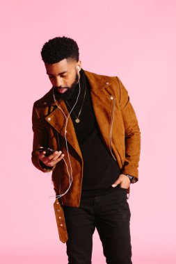 Müzik dinlemek, telefon, pembe studio arka plan üzerinde izole bakarak yakışıklı ve serin Afro-Amerikan sakallı adam,