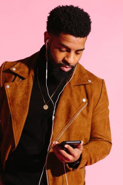 Müzik dinlemek, telefon, pembe studio arka plan üzerinde izole bakarak yakışıklı ve serin Afro-Amerikan sakallı adam,