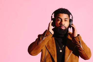 Müzik dinlemek, kamera, pembe studio arka plan üzerinde izole bakarak yakışıklı ve serin Afro-Amerikan sakallı adam,