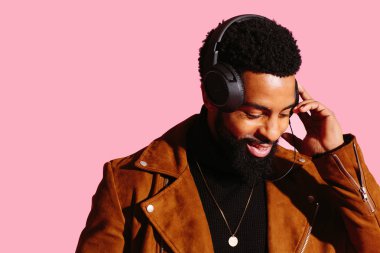 Pembe studio arka planda müzik dinlemek aşağı bakan gülümseyen birisi sakal ve kulaklık ile portresi izole