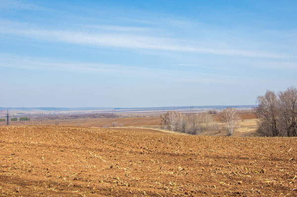 Spring landscape. Freshly plowed field. hilly terrain. trees without leaves. Multicolored spring trees. Snow left over from last year's winter. The last snow.