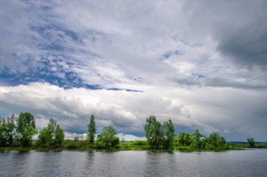Yaz fotoğrafı, güçlü gök gürültülü bulutlar, mavi gökyüzü, karanlık keskin su, Kama Nehri boyunca turist yürüyüşü.