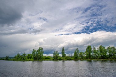 Yaz fotoğrafı, güçlü gök gürültülü bulutlar, mavi gökyüzü, karanlık keskin su, Kama Nehri boyunca turist yürüyüşü.