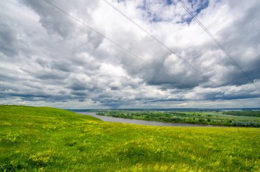 Yaz manzarası, büyük bir nehir, nehrin kıyısında çayır çiçekleri, gökyüzünde güçlü bulutlar, Kama Nehri boyunca bir turist yürüyüşü.