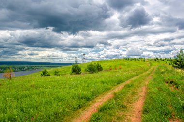 Yaz manzarası, büyük bir nehir, nehrin kıyısında çayır çiçekleri, gökyüzünde güçlü bulutlar, Kama Nehri boyunca bir turist yürüyüşü.