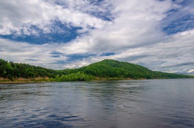 Yaz fotoğrafı, güçlü gök gürültülü bulutlar, mavi gökyüzü, karanlık keskin su, Kama Nehri boyunca turist yürüyüşü.