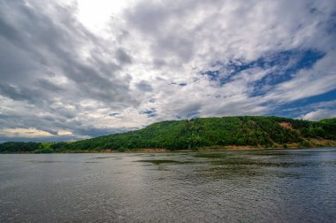 Yaz fotoğrafı, güçlü gök gürültülü bulutlar, mavi gökyüzü, karanlık keskin su, Kama Nehri boyunca turist yürüyüşü.