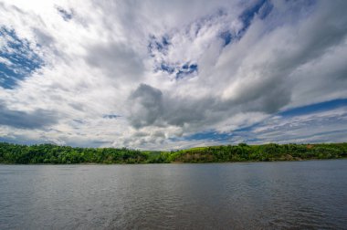 Yaz fotoğrafı, güçlü gök gürültülü bulutlar, mavi gökyüzü, karanlık keskin su, Kama Nehri boyunca turist yürüyüşü.