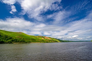 Yaz fotoğrafı, güçlü gök gürültülü bulutlar, mavi gökyüzü, karanlık keskin su, Kama Nehri boyunca turist yürüyüşü.