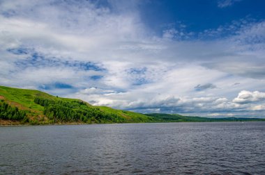 Yaz fotoğrafı, güçlü gök gürültülü bulutlar, mavi gökyüzü, karanlık keskin su, Kama Nehri boyunca turist yürüyüşü.