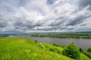 Yaz manzarası, büyük bir nehir, nehrin kıyısında çayır çiçekleri, gökyüzünde güçlü bulutlar, Kama Nehri boyunca bir turist yürüyüşü.