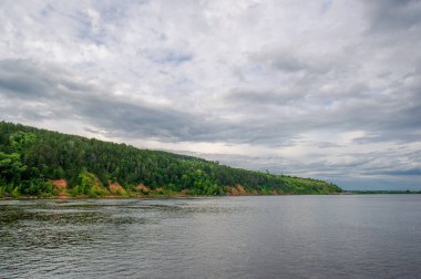 Yaz fotoğrafı, güçlü gök gürültülü bulutlar, mavi gökyüzü, karanlık keskin su, Kama Nehri boyunca turist yürüyüşü.