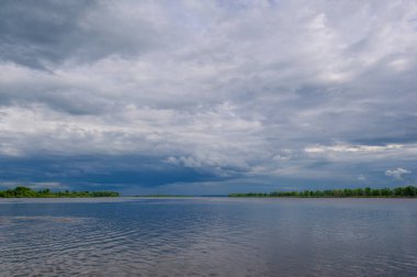 Yaz fotoğrafı, güçlü gök gürültülü bulutlar, mavi gökyüzü, karanlık keskin su, Kama Nehri boyunca turist yürüyüşü.