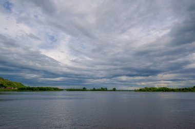 Yaz fotoğrafı, güçlü gök gürültülü bulutlar, mavi gökyüzü, karanlık keskin su, Kama Nehri boyunca turist yürüyüşü.