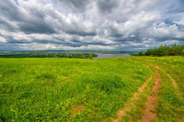 Yaz manzarası, büyük bir nehir, nehrin kıyısında çayır çiçekleri, gökyüzünde güçlü bulutlar, Kama Nehri boyunca bir turist yürüyüşü.