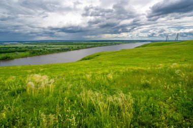 Yaz manzarası, büyük bir nehir, nehrin kıyısında çayır çiçekleri, gökyüzünde güçlü bulutlar, Kama Nehri boyunca bir turist yürüyüşü.