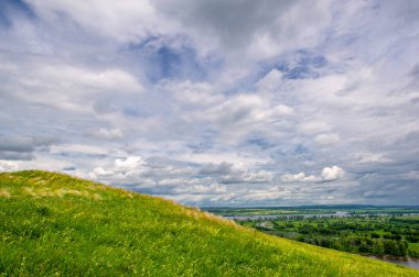 Yaz manzarası, büyük bir nehir, nehrin kıyısında çayır çiçekleri, gökyüzünde güçlü bulutlar, Kama Nehri boyunca bir turist yürüyüşü.