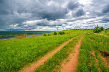 Yaz manzarası, büyük bir nehir, nehrin kıyısında çayır çiçekleri, gökyüzünde güçlü bulutlar, Kama Nehri boyunca bir turist yürüyüşü.