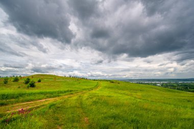 Yaz manzarası, büyük bir nehir, nehrin kıyısında çayır çiçekleri, gökyüzünde güçlü bulutlar, Kama Nehri boyunca bir turist yürüyüşü.